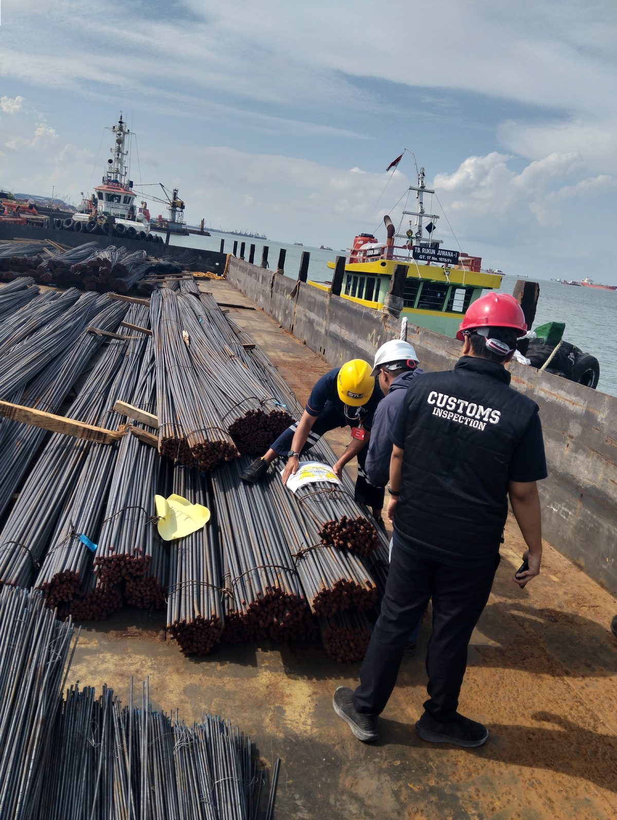 Helmeted officers inspecting stacked rebar aboard a barge