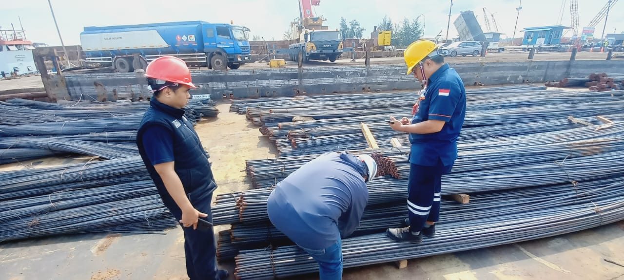 Three officers inspecting rebar at a dockside area