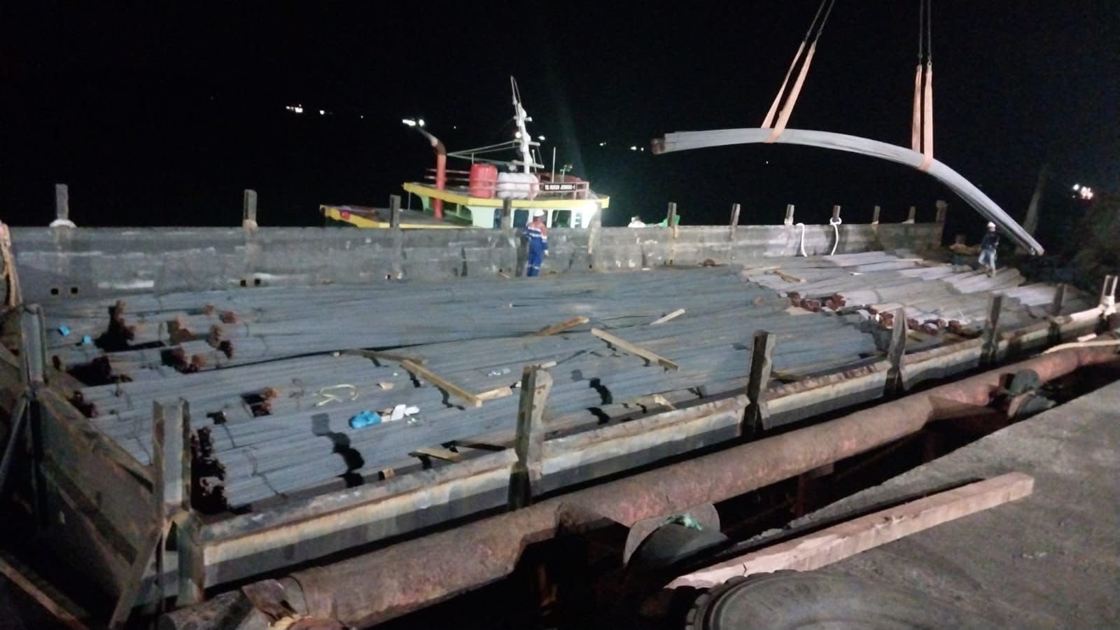 A barge being loaded with steel rebar at night via crane