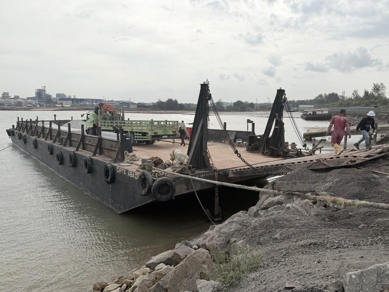 A barge alongside a dock with a crane truck on deck